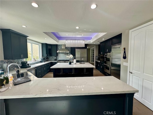 kitchen with tasteful backsplash, wall chimney range hood, a center island, a raised ceiling, and appliances with stainless steel finishes