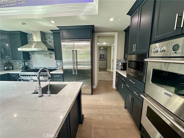 kitchen featuring sink, built in appliances, light hardwood / wood-style flooring, light stone countertops, and wall chimney exhaust hood