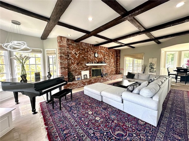 living room featuring a brick fireplace, brick wall, a healthy amount of sunlight, and beam ceiling