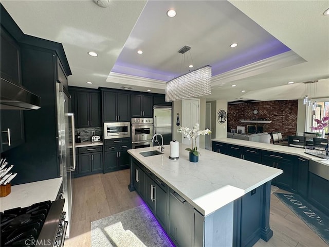 kitchen featuring pendant lighting, a raised ceiling, a large island, and built in appliances