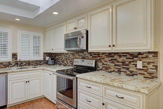 kitchen with appliances with stainless steel finishes, sink, light stone counters, and cream cabinets