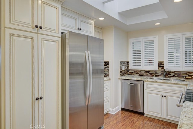 kitchen with stainless steel appliances, light hardwood / wood-style flooring, light stone counters, and sink