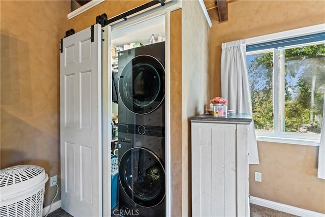 clothes washing area featuring carpet floors, a barn door, stacked washer and dryer, and a wealth of natural light