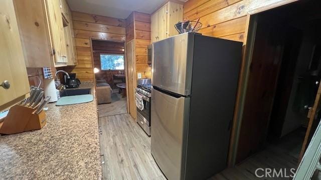 kitchen featuring wood walls, appliances with stainless steel finishes, light wood-type flooring, light brown cabinetry, and sink