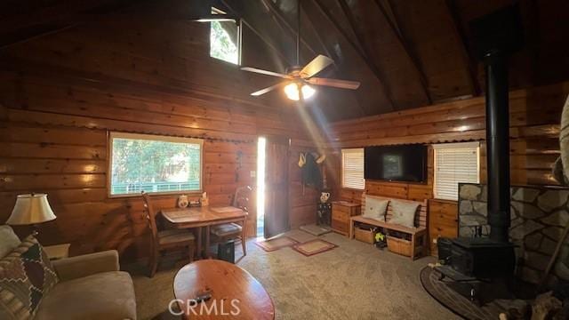 carpeted living room with wood walls, plenty of natural light, a wood stove, and beam ceiling