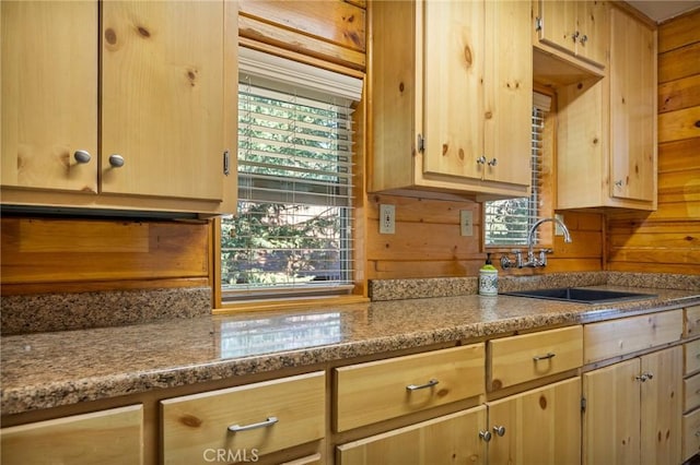 kitchen featuring light stone counters, sink, light brown cabinets, and wood walls