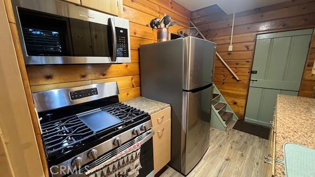 kitchen with light wood-type flooring, green cabinets, wooden walls, and stainless steel appliances