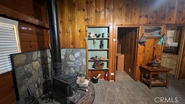 interior space featuring carpet, wooden walls, and a wood stove