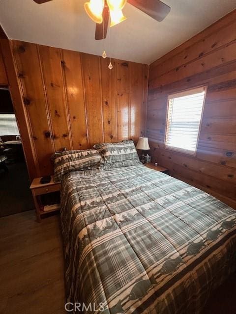 bedroom featuring ceiling fan, dark hardwood / wood-style flooring, and wood walls