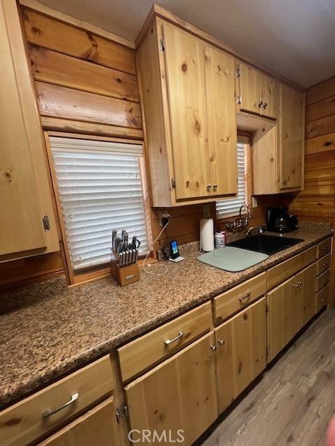 kitchen with light brown cabinets, sink, wooden walls, and light hardwood / wood-style floors