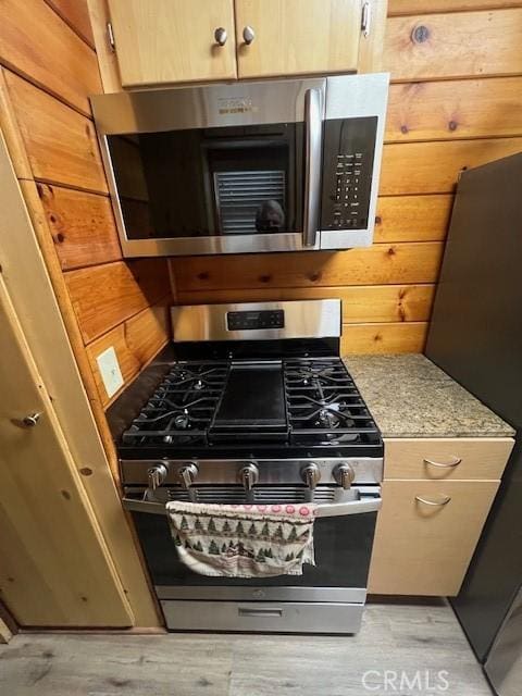 kitchen with appliances with stainless steel finishes, light wood-type flooring, and wooden walls