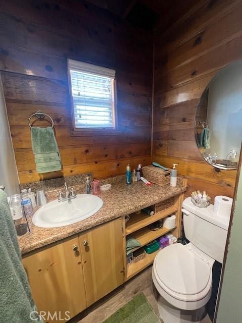 bathroom with toilet, vanity, and wooden walls