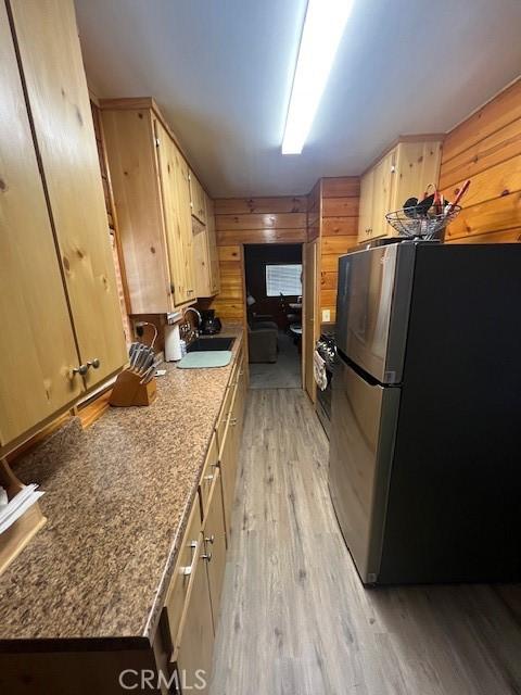 kitchen with wooden walls, light brown cabinetry, stainless steel refrigerator, light hardwood / wood-style flooring, and sink