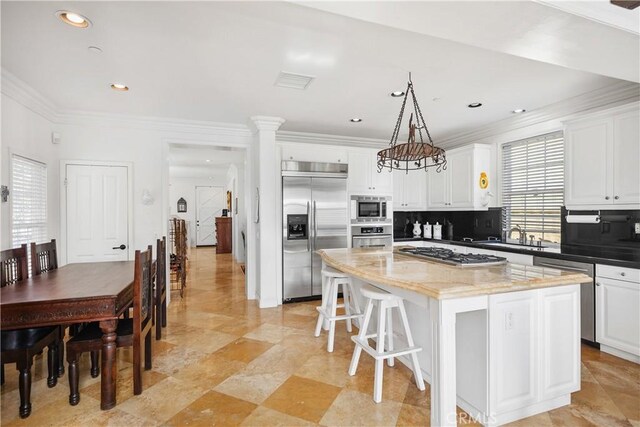 kitchen with decorative light fixtures, dark stone countertops, built in appliances, a kitchen island, and white cabinets