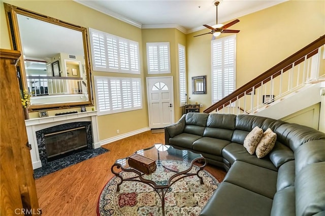 living room with ceiling fan, ornamental molding, a high end fireplace, and wood-type flooring