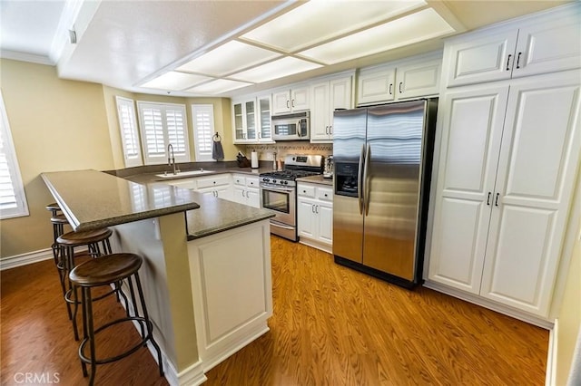 kitchen with light hardwood / wood-style flooring, a breakfast bar, appliances with stainless steel finishes, white cabinets, and kitchen peninsula