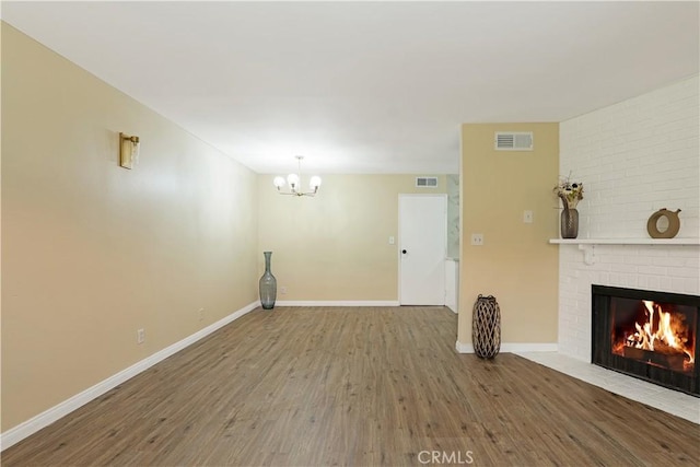 unfurnished living room featuring a brick fireplace, wood-type flooring, and a notable chandelier