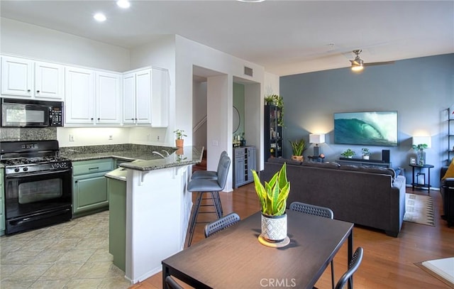 kitchen featuring kitchen peninsula, dark stone countertops, white cabinets, a breakfast bar, and black appliances