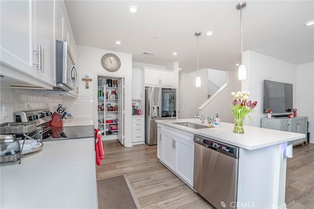 kitchen with pendant lighting, white cabinets, stainless steel appliances, an island with sink, and sink