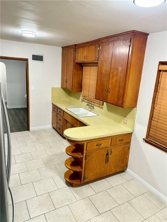 kitchen with tasteful backsplash, sink, light tile patterned floors, and stainless steel refrigerator