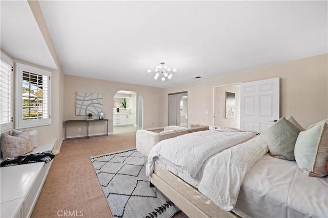 bedroom with ensuite bath, light carpet, a closet, and an inviting chandelier