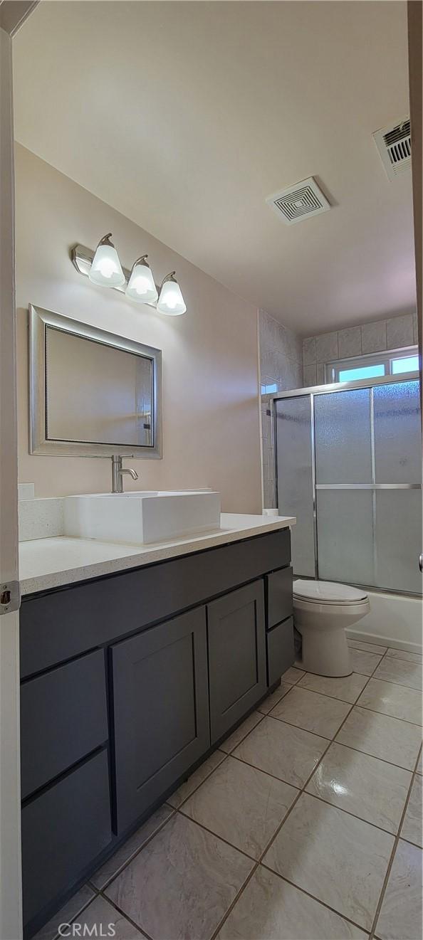 full bathroom featuring toilet, bath / shower combo with glass door, tile patterned flooring, and vanity