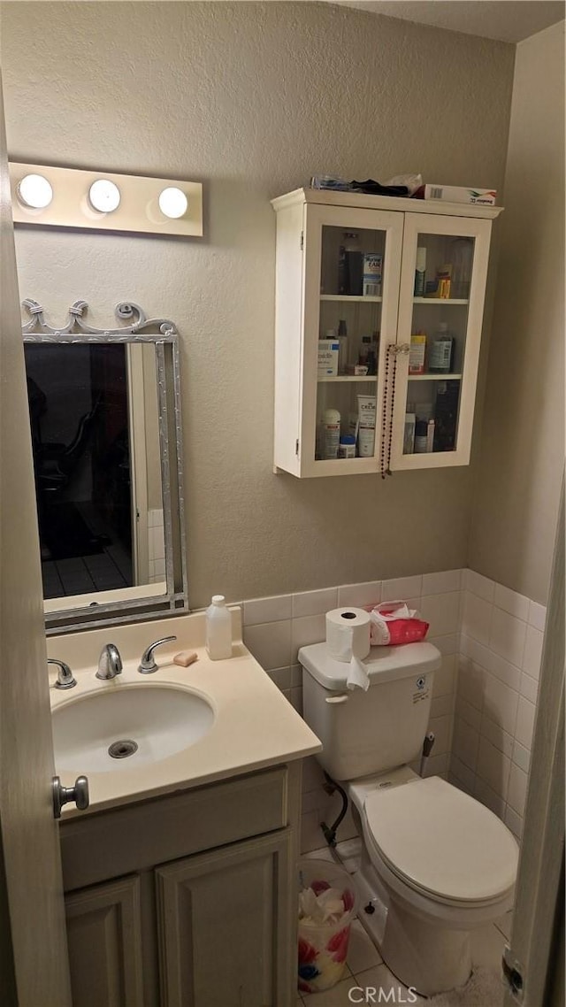 bathroom with a textured ceiling, tile patterned floors, vanity, tile walls, and toilet