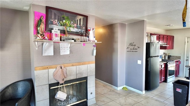 kitchen with a fireplace, refrigerator, a textured ceiling, light tile patterned floors, and gas range