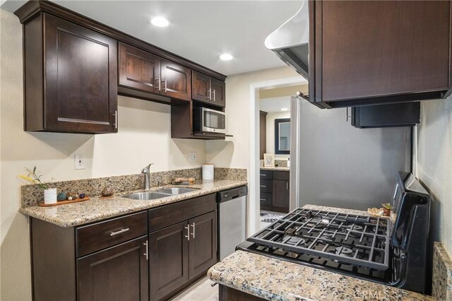 kitchen with light stone countertops, sink, appliances with stainless steel finishes, and dark brown cabinets