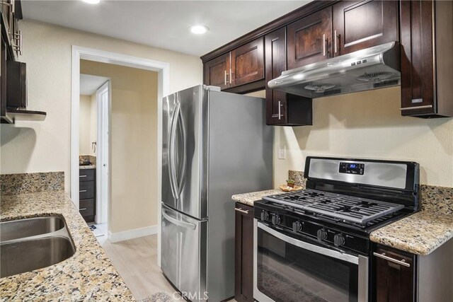 kitchen featuring sink, light wood-type flooring, light stone countertops, stainless steel appliances, and dark brown cabinets