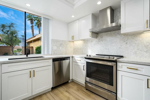 kitchen featuring sink, white cabinetry, light hardwood / wood-style flooring, wall chimney range hood, and appliances with stainless steel finishes