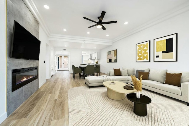 living room featuring ceiling fan, light wood-type flooring, a tiled fireplace, and ornamental molding