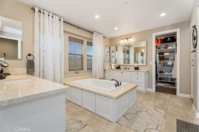 bathroom with a sink, a garden tub, a spacious closet, two vanities, and recessed lighting