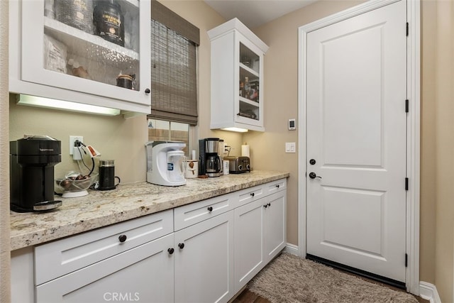 kitchen featuring glass insert cabinets, baseboards, white cabinets, and light stone counters