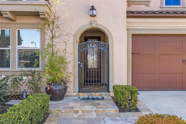 view of exterior entry with a garage, a tiled roof, and stucco siding