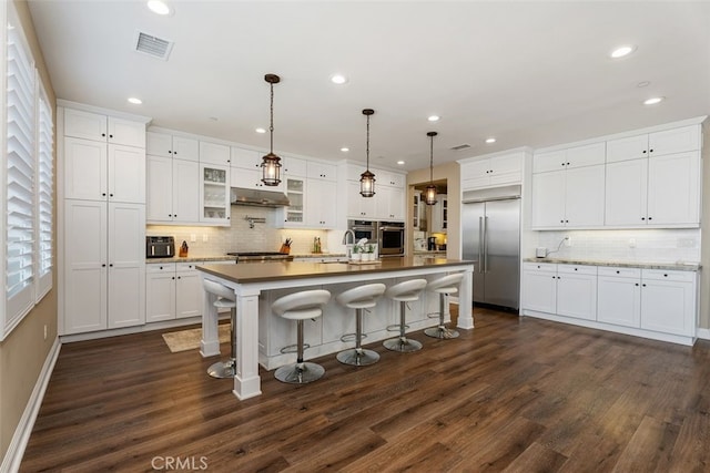 kitchen with white cabinets, stainless steel appliances, a kitchen breakfast bar, and an island with sink