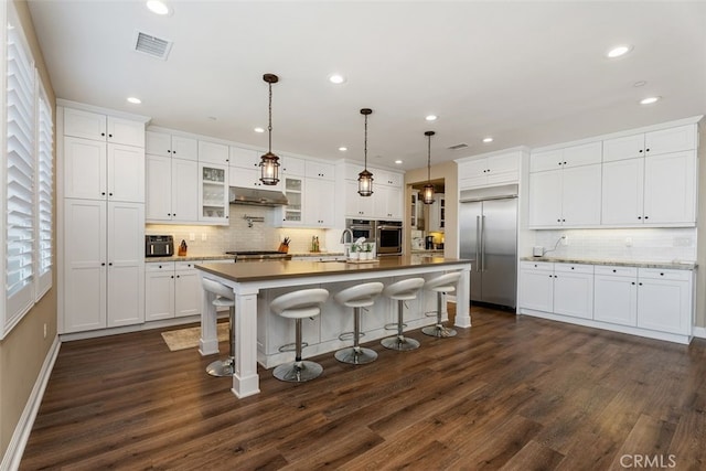 kitchen featuring dark wood-style flooring, visible vents, appliances with stainless steel finishes, white cabinets, and under cabinet range hood