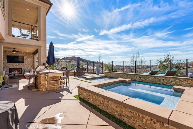 view of swimming pool with a patio, outdoor dry bar, an in ground hot tub, a lit fireplace, and fence