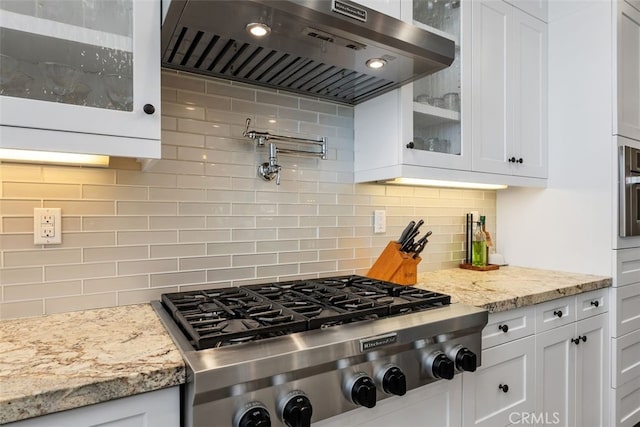 kitchen with wall chimney exhaust hood, glass insert cabinets, white cabinetry, and stainless steel gas stovetop