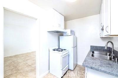 kitchen with light stone counters, sink, white appliances, and white cabinets