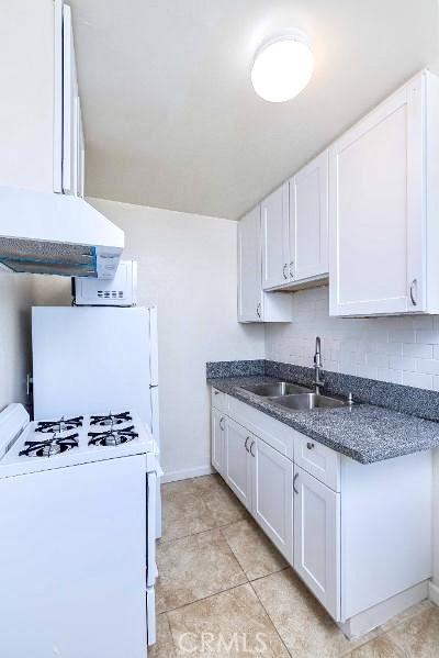 kitchen with sink, white appliances, white cabinets, and range hood