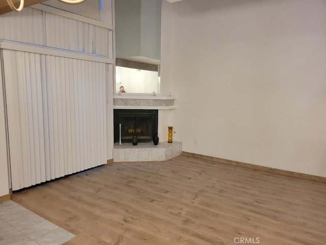 unfurnished living room with a high ceiling, a tile fireplace, wood finished floors, and baseboards