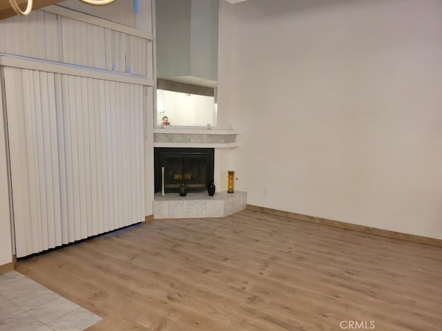 unfurnished living room with baseboards, a high ceiling, a fireplace with raised hearth, and wood finished floors