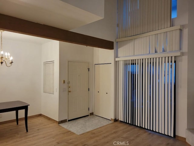 entryway featuring baseboards, wood finished floors, beam ceiling, and an inviting chandelier