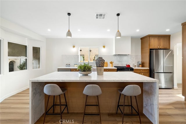 kitchen with a breakfast bar, light stone counters, decorative light fixtures, stainless steel appliances, and decorative backsplash