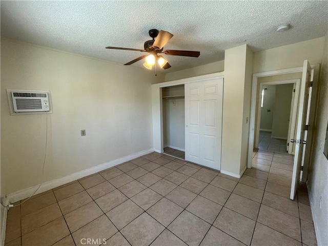 unfurnished bedroom with an AC wall unit, a textured ceiling, a closet, ceiling fan, and light tile patterned floors