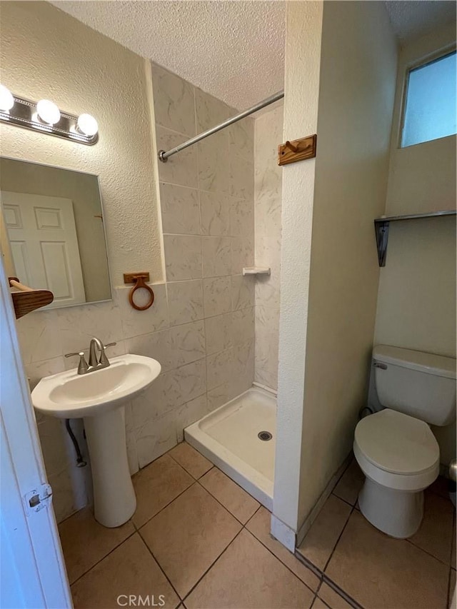 bathroom featuring a textured ceiling, tiled shower, toilet, and tile patterned flooring