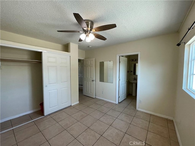 unfurnished bedroom featuring a textured ceiling, ensuite bath, a closet, light tile patterned flooring, and ceiling fan