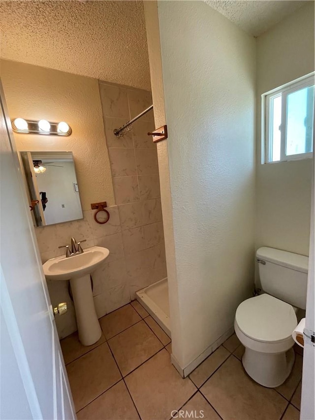 bathroom featuring toilet, a tile shower, a textured ceiling, and tile patterned flooring