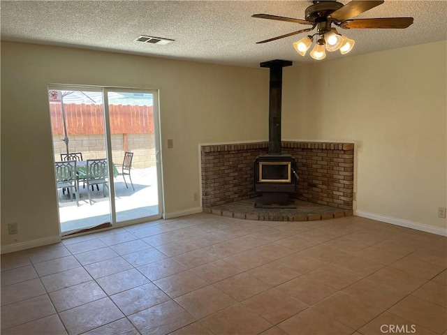 unfurnished living room featuring ceiling fan, a wood stove, a textured ceiling, and light tile patterned floors